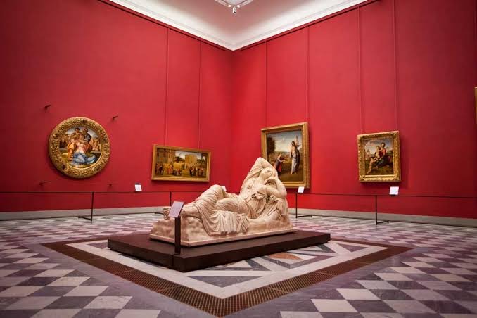 Sala dalle pareti rosse dentro la Galleria degli Uffizi con la scultura dell'Arianna addormentata